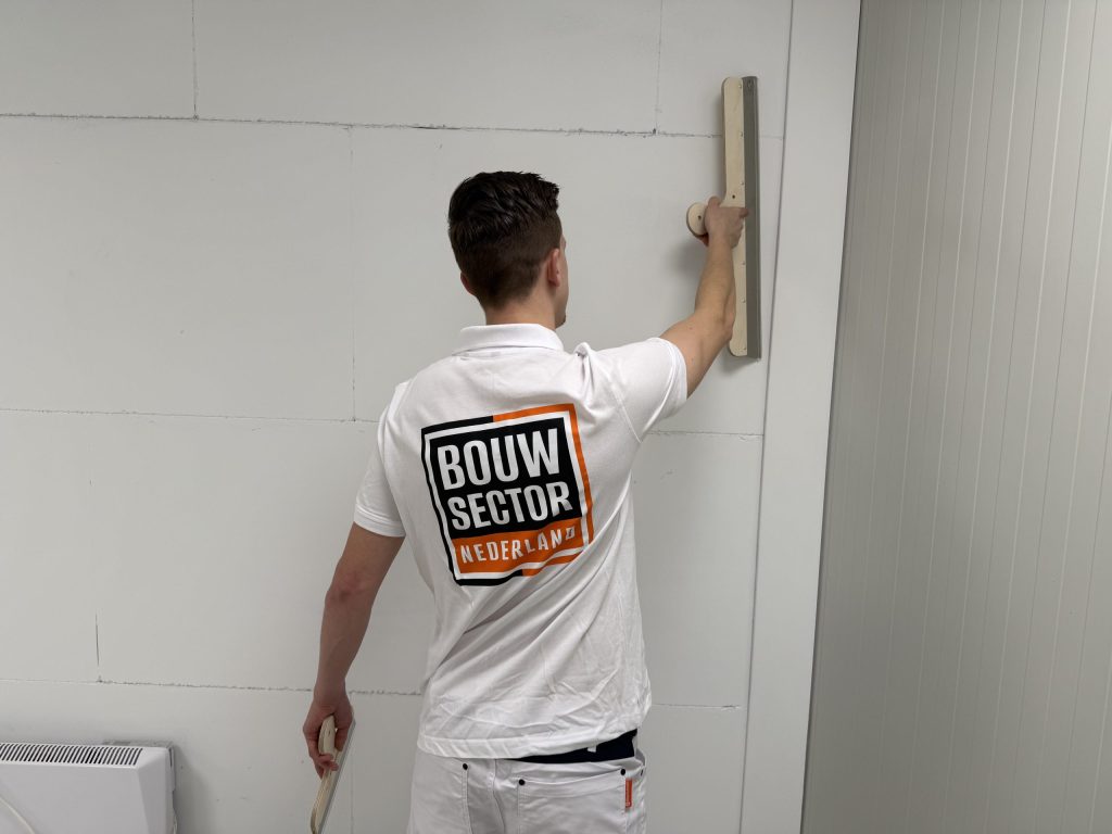 Stukadoor van Bouwsector Nederland trekt met een lange spaan een verse laag over een wand