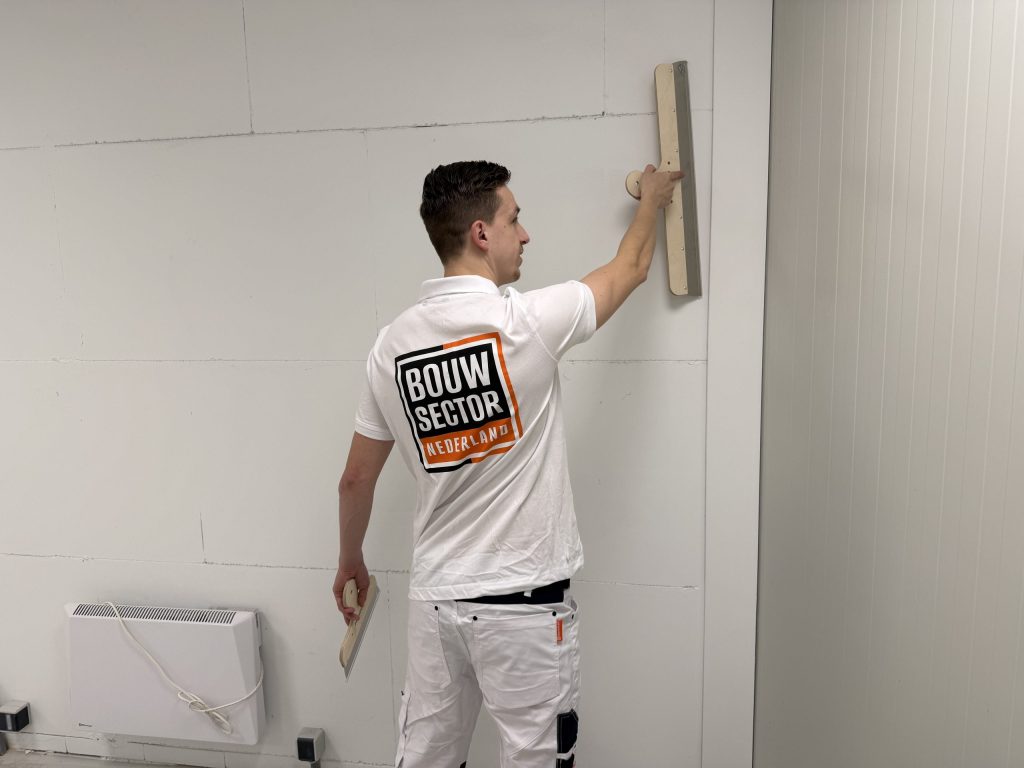 Vakman van Bouwsector Nederland met spaan en plakspaan aan een wand van gipsplaat naast een radiator
