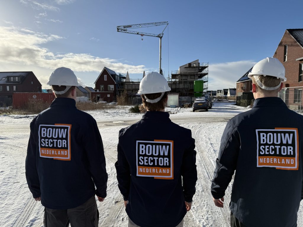 Teamleden van Bouwsector Nederland in bedrijfskleding kijken uit over huizen in aanbouw