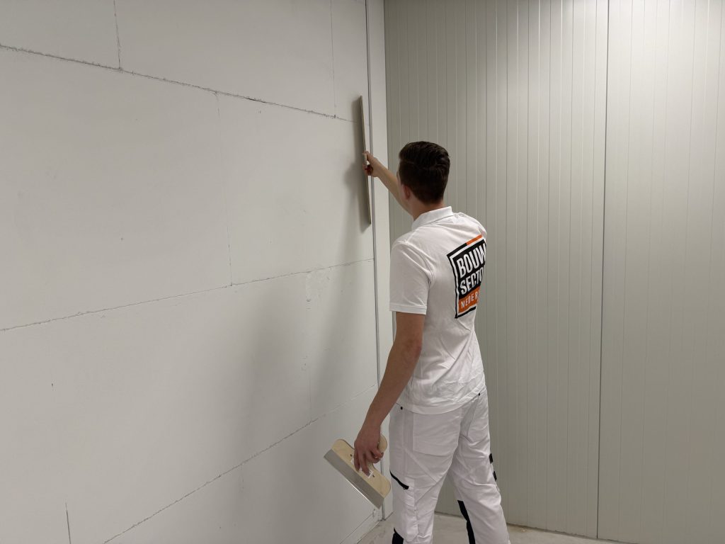 Stukadoor zet een lange spaan verticaal tegen de wand bij een binnenhoek om de laag vlak te trekken